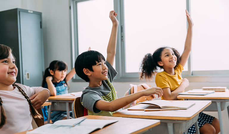 Children in class raising their hands to answer a question